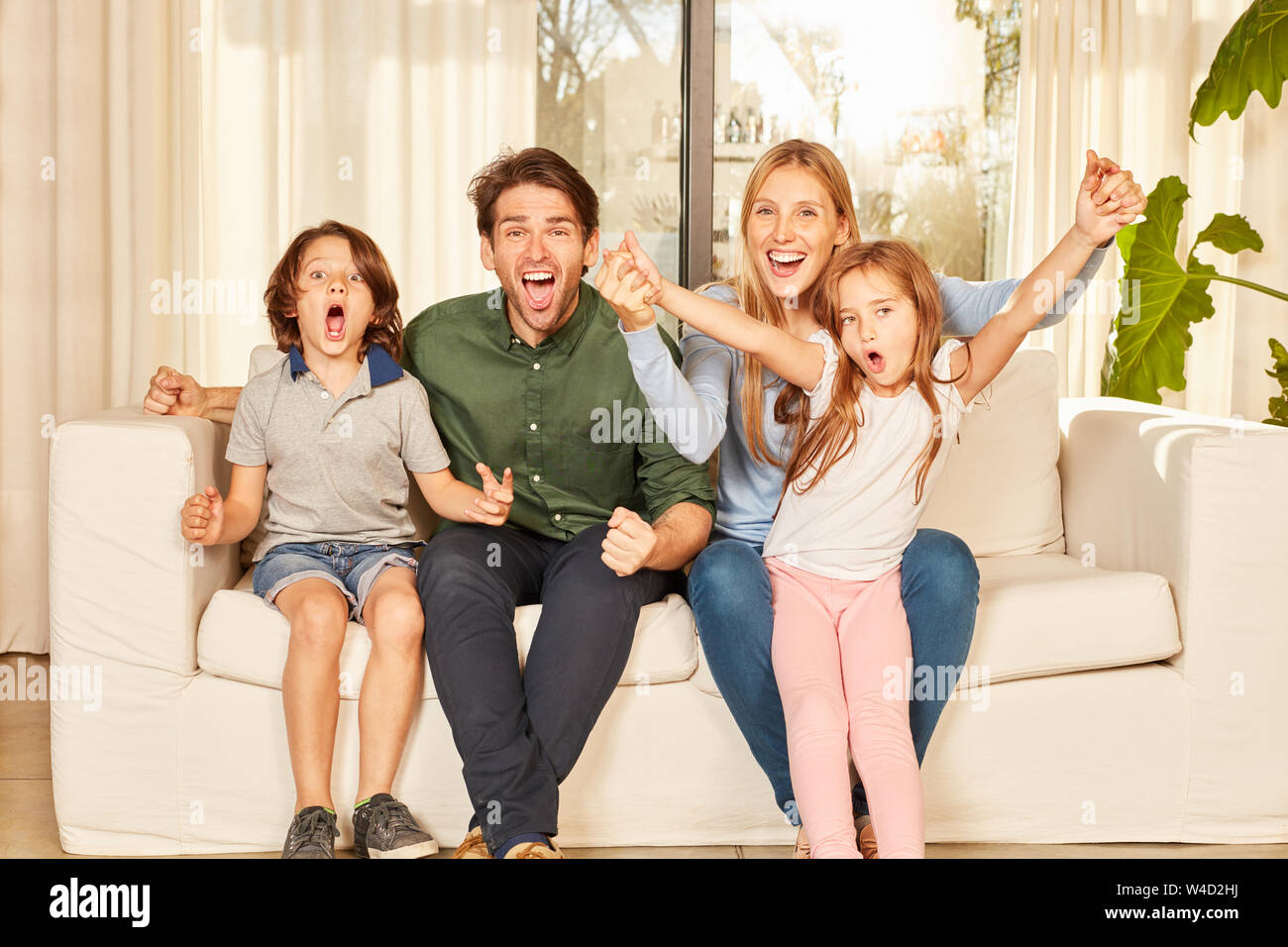 Jubelnde Familie mit zwei Kindern auf dem Sofa in der neuen Wohnung Stockfoto