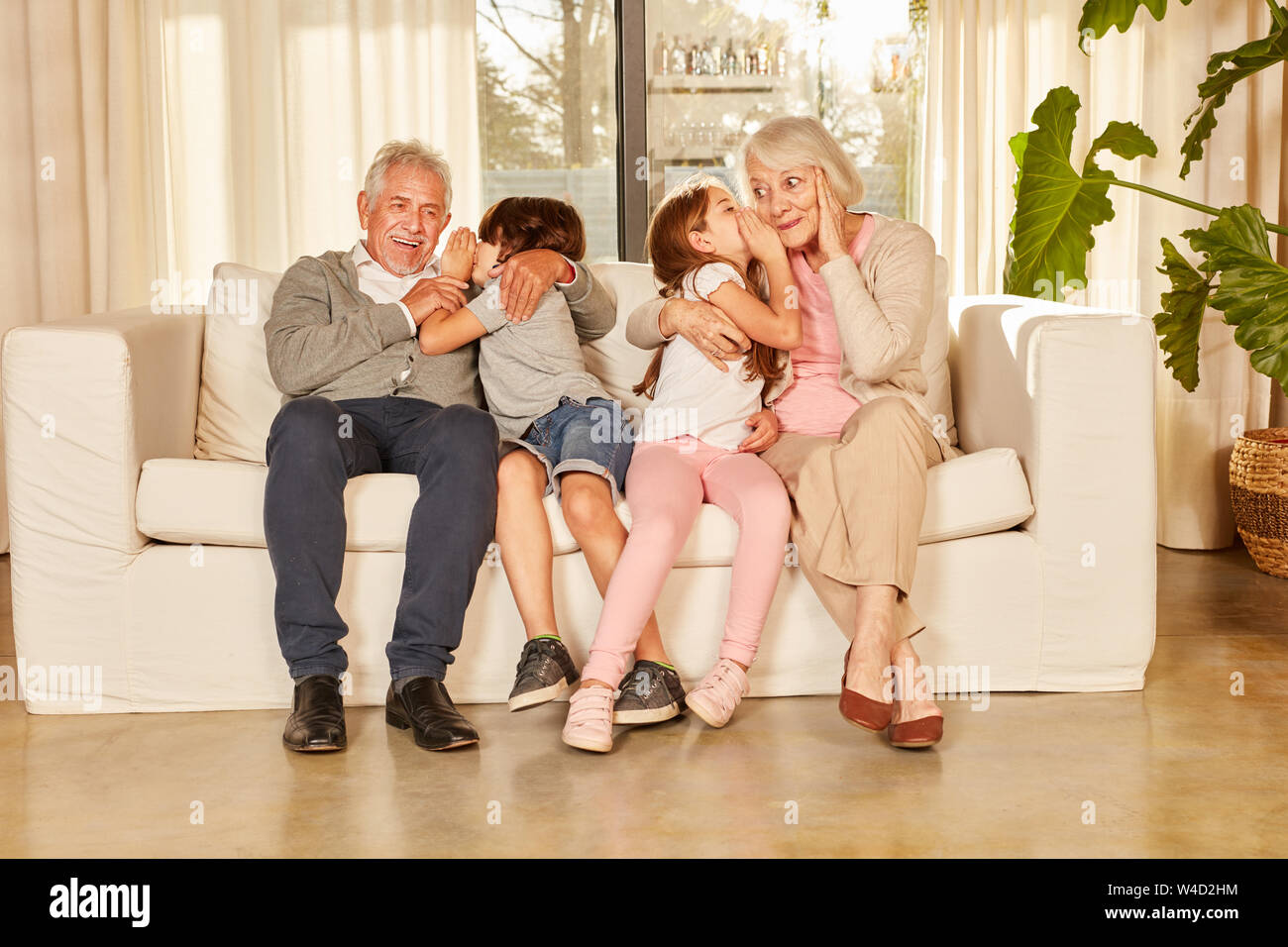 Enkel Flüstern ein Geheimnis in den Ohren auf dem Sofa zu Hause zu ihren Großeltern Stockfoto