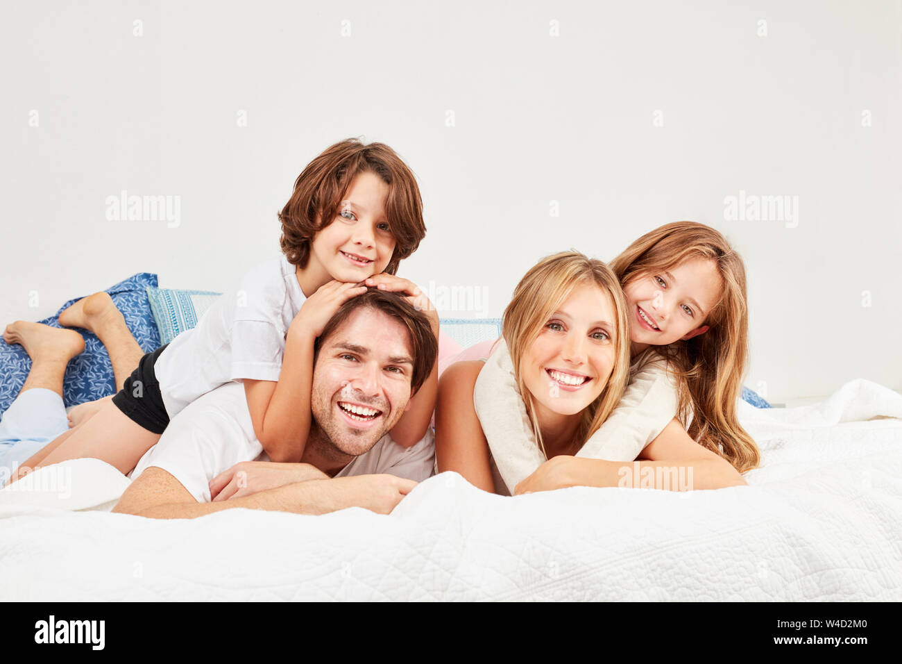 Glückliche Eltern und ihre zwei Kinder am Morgen zusammen im Bett im Schlafzimmer Stockfoto