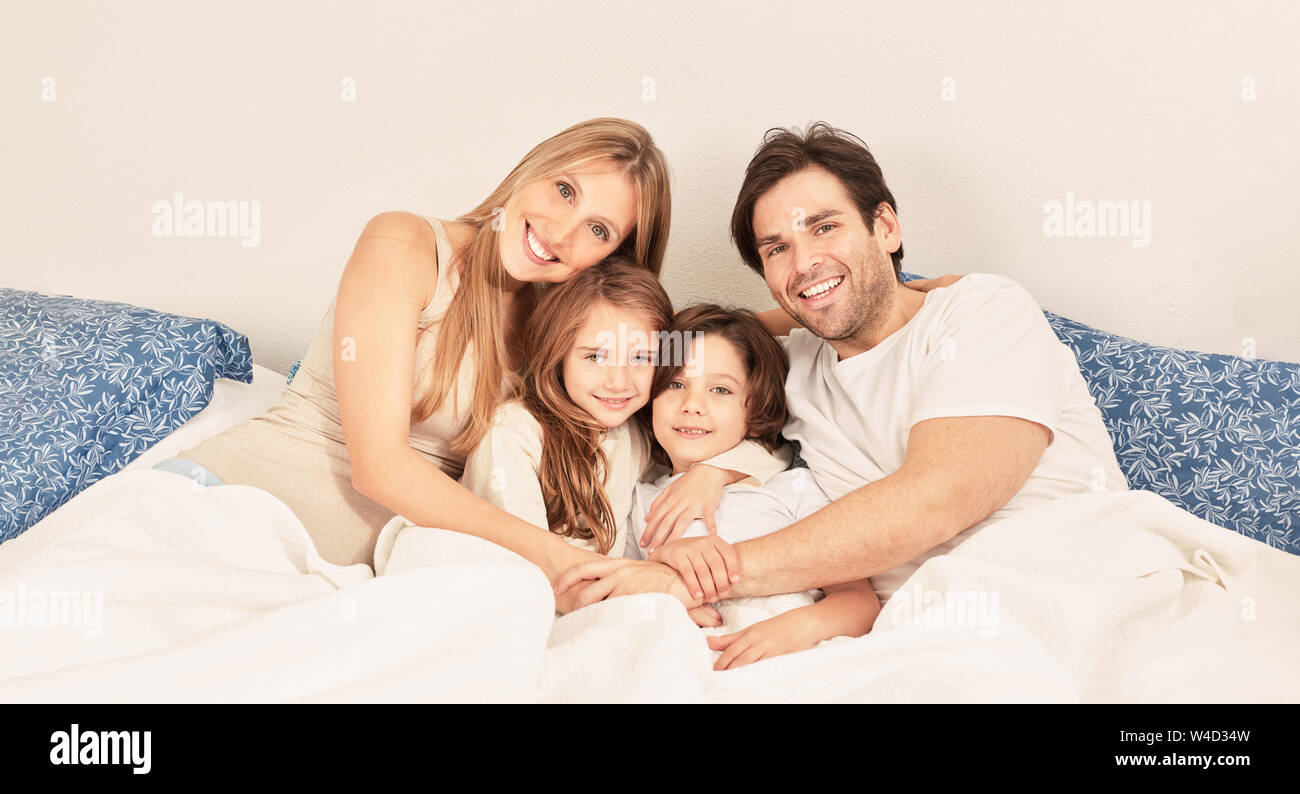 Glückliche Familie mit zwei Kindern kuscheln im Bett als Header Stockfoto