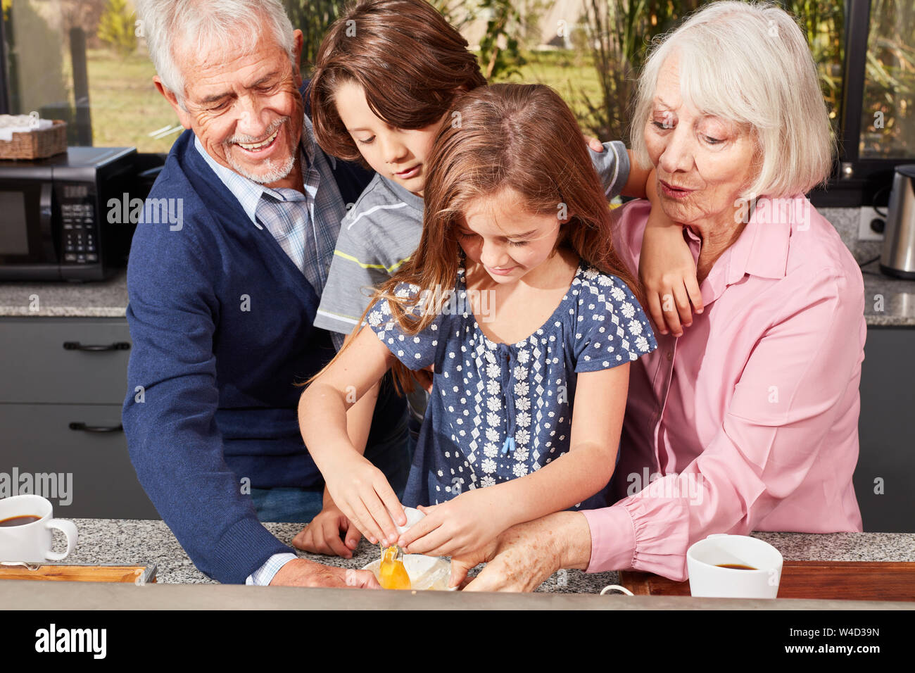 Zwei Kinder backen Pizza mit den beiden Großeltern in der Küche Stockfoto