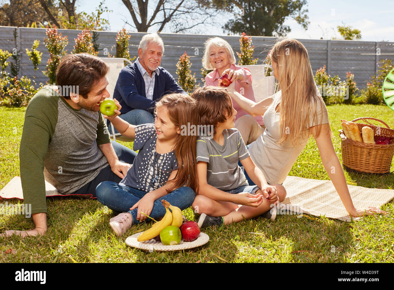 Glückliche Familie mit Kindern und Großeltern bei einem Picknick mit Obst im Garten Stockfoto