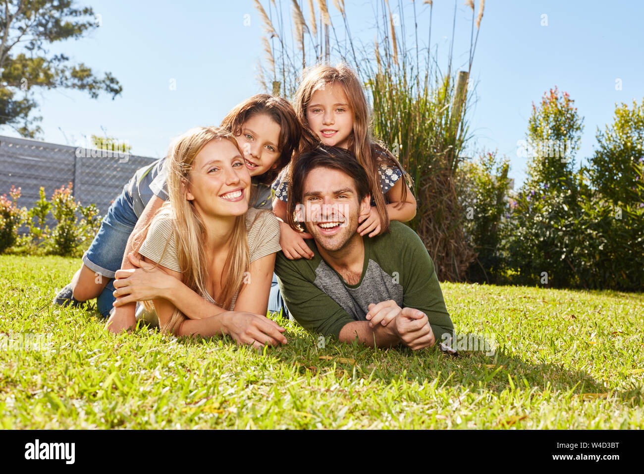 Glückliche Eltern und zwei Kindern zusammen liegen auf einer Wiese im Sommer Stockfoto