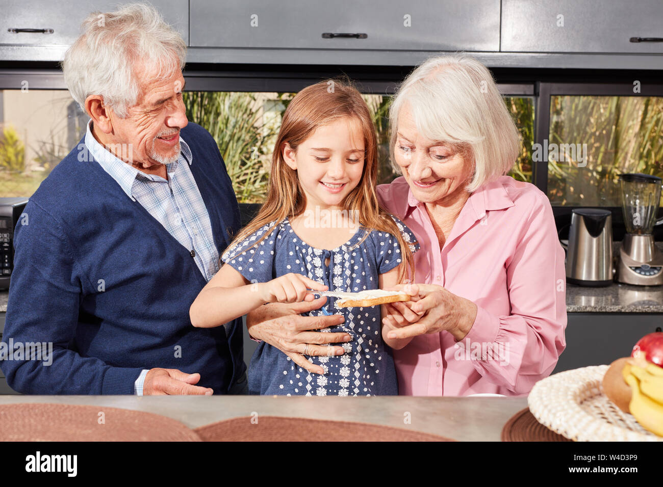 Großeltern und Mädchen als Enkelin bestreichen Brot für das Frühstück Stockfoto