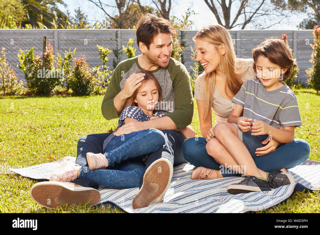 Glückliche Eltern mit zwei Kindern Sitzen im Garten im Sommer auf der Picknickdecke Stockfoto