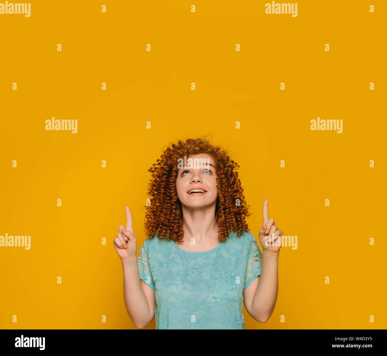 Suchen höher. Frau mit Locken zeigende Hand bis auf gelbem Hintergrund Stockfoto