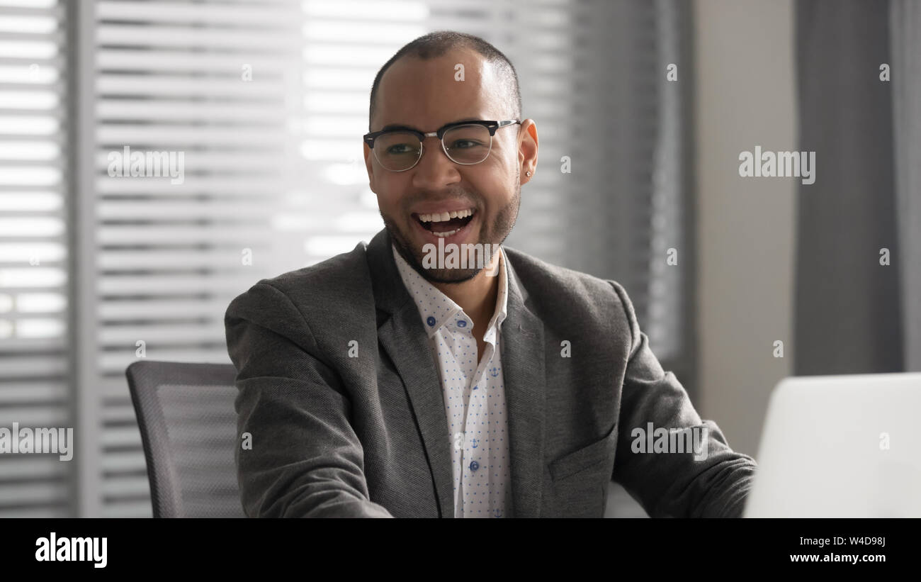 Positiven afrikanischen Geschäftsmann in Anzug lachend Sitzen am Schreibtisch Stockfoto