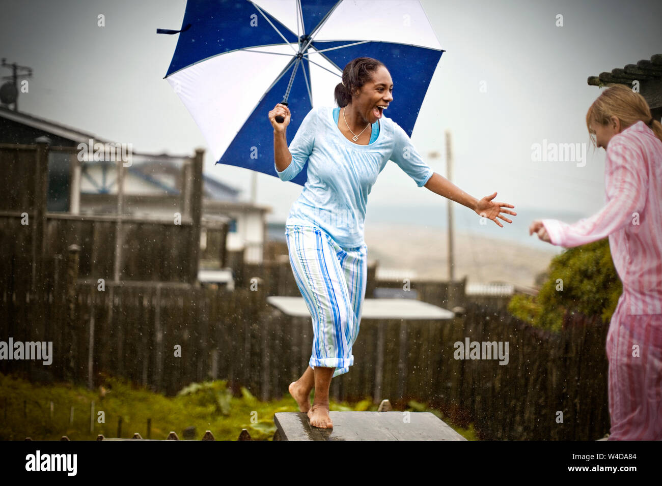 Zwei Lachende junge Frauen Spaß haben Ihren Pyjamas tragen, während draußen im Regen mit einem Schirm stehen. Stockfoto