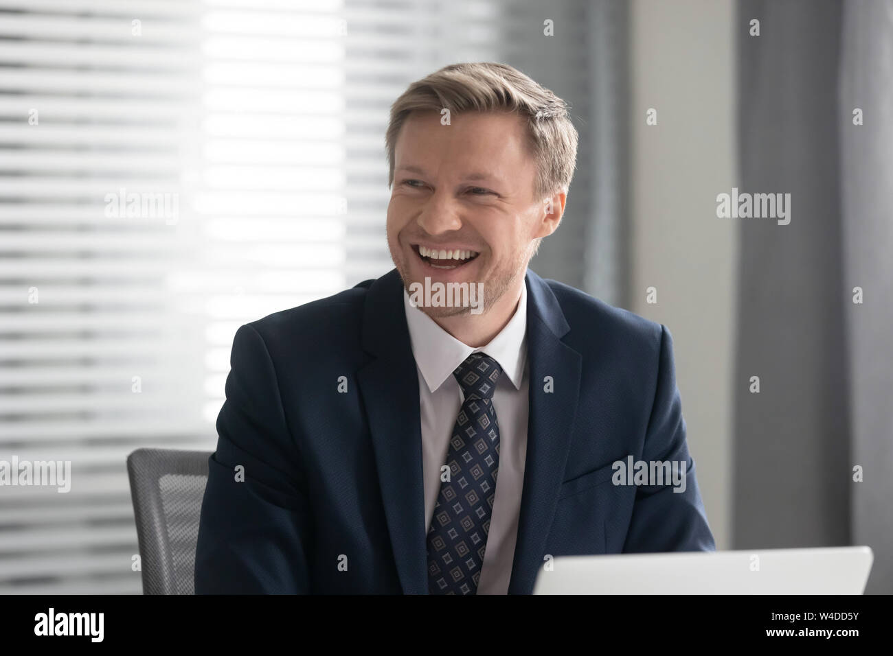 Gerne fröhliche Geschäftsmann in Anzug lachend Sitzen am Schreibtisch Stockfoto