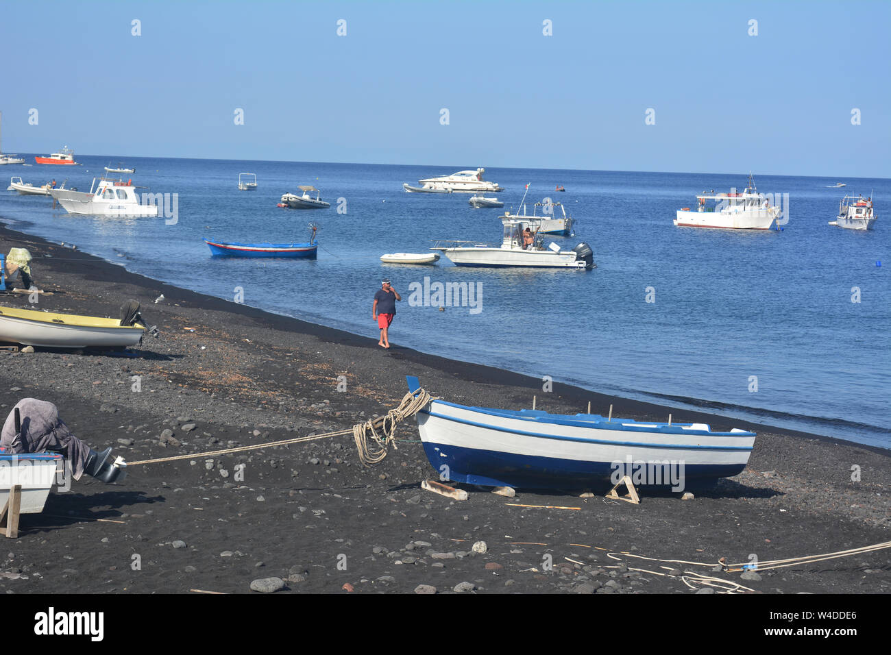 Seascape der natürlichen Wunder und UNESCO-Weltkulturerbe - Stromboli vulkanischen Strand in Italien. Man Walking und über sein Telefon von Fischerboote umgeben Stockfoto