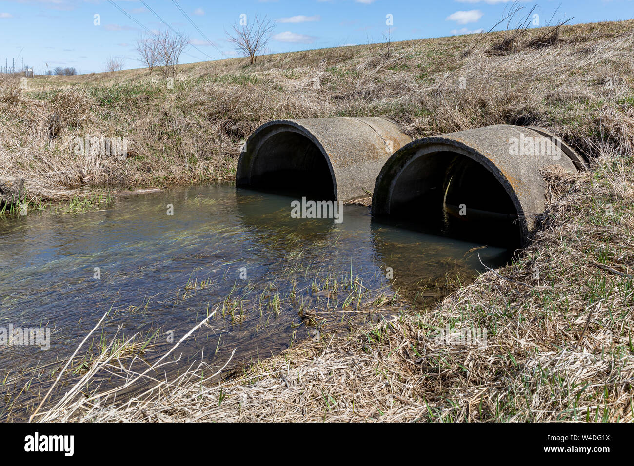 Ablaufendes Regenwasser fließt von Entwässerungsgraben in konkrete Durchlässe unter einer Straße Stockfoto