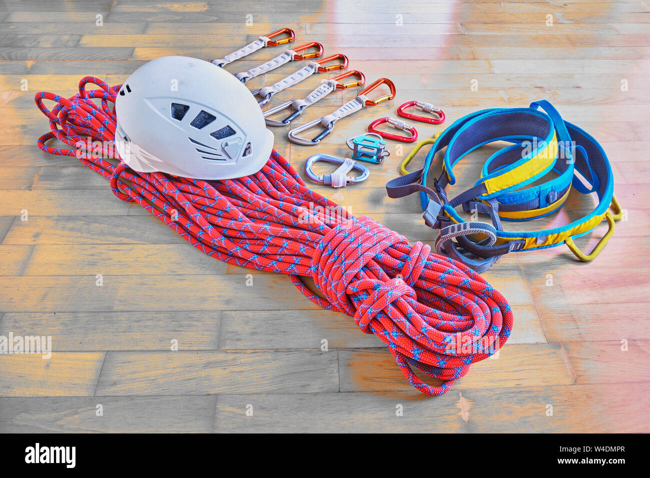 Kletterausrüstung auf hölzernen Hintergrund: rot dynamisches Seil mit blauen Streifen, Helm, blau/gelben Kabelbaum, Expressschlingen, Belay Device mit HMS Karabiner, Stockfoto