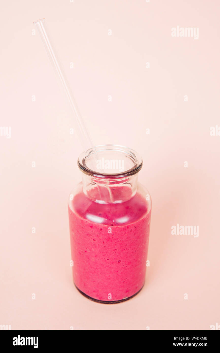 Minimalistische Komposition aus Glas mit Himbeer Smoothie und mit wiederverwendbaren Glas Stroh auf rosa Hintergrund Stockfoto