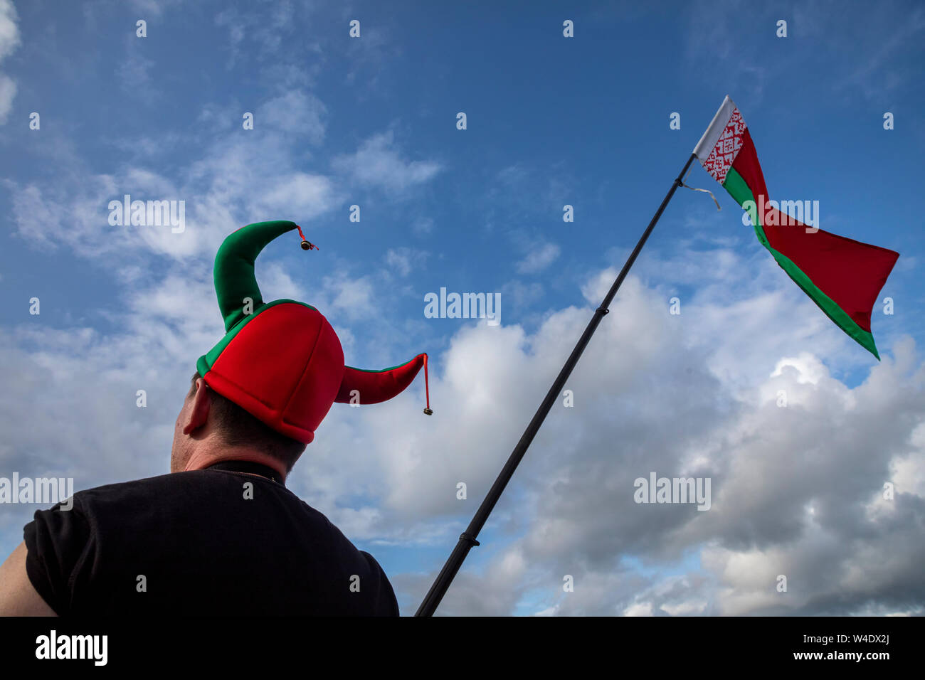 Ein Ventilator in eine Kappe der Farben des weißrussischen Flagge und mit der Nationalflagge der Republik Belarus geht eine Straße Stockfoto