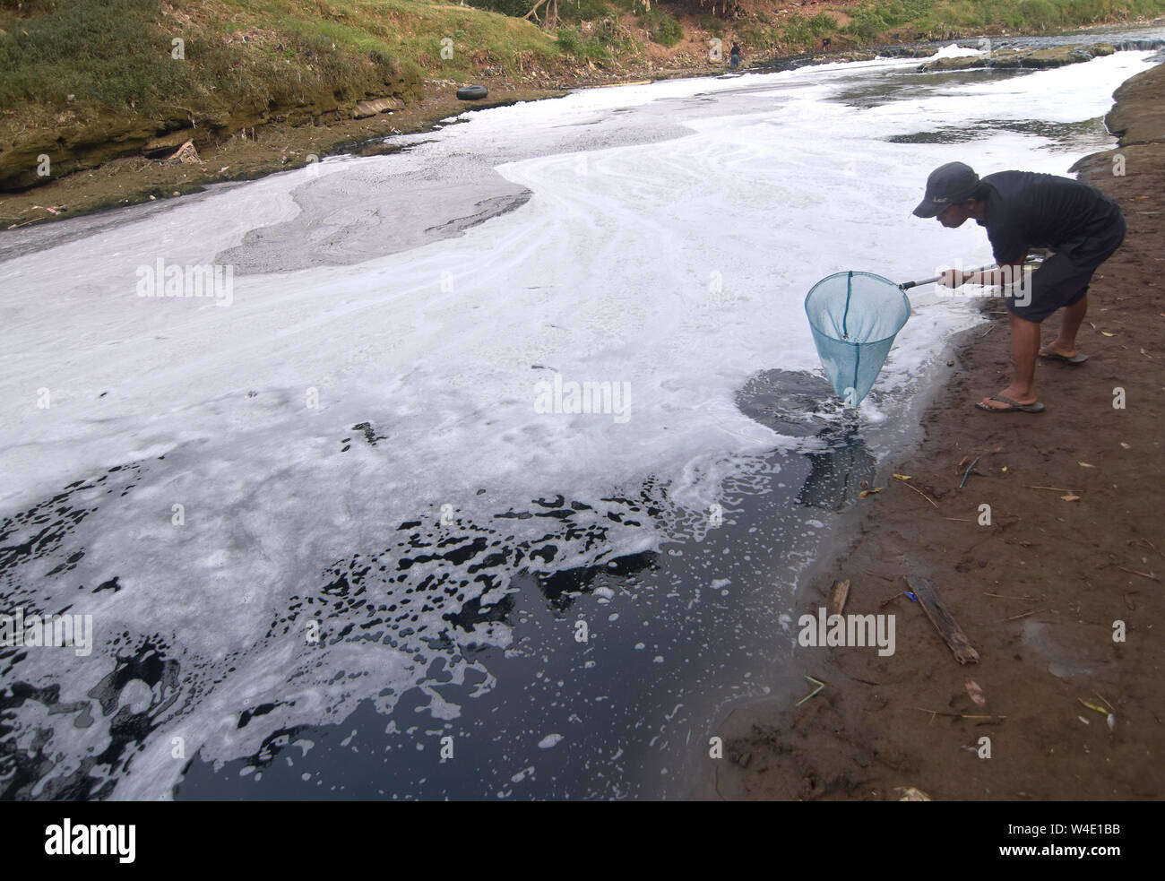 Juli 22, 2019 - Bogor, Jawa Barat, Indonesien - ein Mann gesehen, Angeln am Fluss Cileungsi beschichtet in Schaum.. Die giftige Industrieabfälle, die von nahe gelegenen Fabriken entleert wird Wasser in einem Fluss schwarz, das Töten von Fischen verursacht und produziert einen fauligen Geruch. (Bild: © agung Fatma Putra/SOPA Bilder über ZUMA Draht) Stockfoto