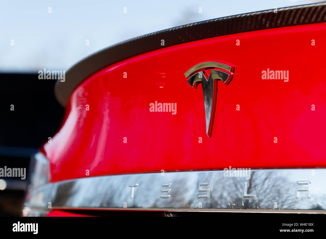 Tesla Emblem auf der Rückseite der roten Tesla Model S scheint auf einem hellen, sonnigen Tag. Stockfoto