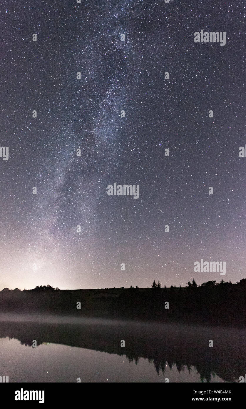 Die Milchstraße, Sterne am Nachthimmel umgeben, die eine Erscheinung über einer nahe gelegenen Stausee während eines kalten Winters nacht Fotografie schießen. Stockfoto