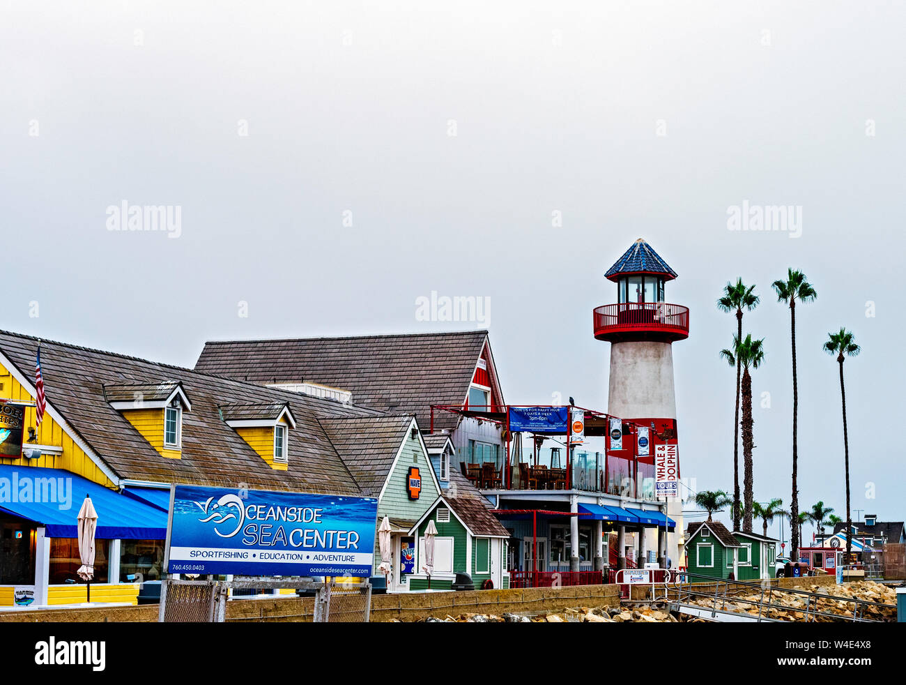 Einkaufszentrum mit roten und weißen Leuchtturm, Palmen und Schilder. Stockfoto