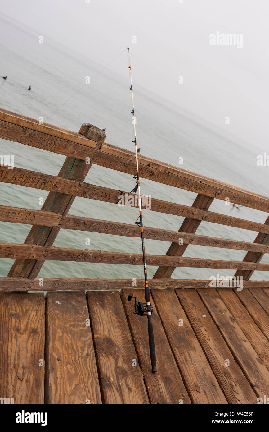 Fishingrod gegen das Holz Pier Geländer lehnend. Ozean darunter Pier an einem nebligen Tag. Stockfoto