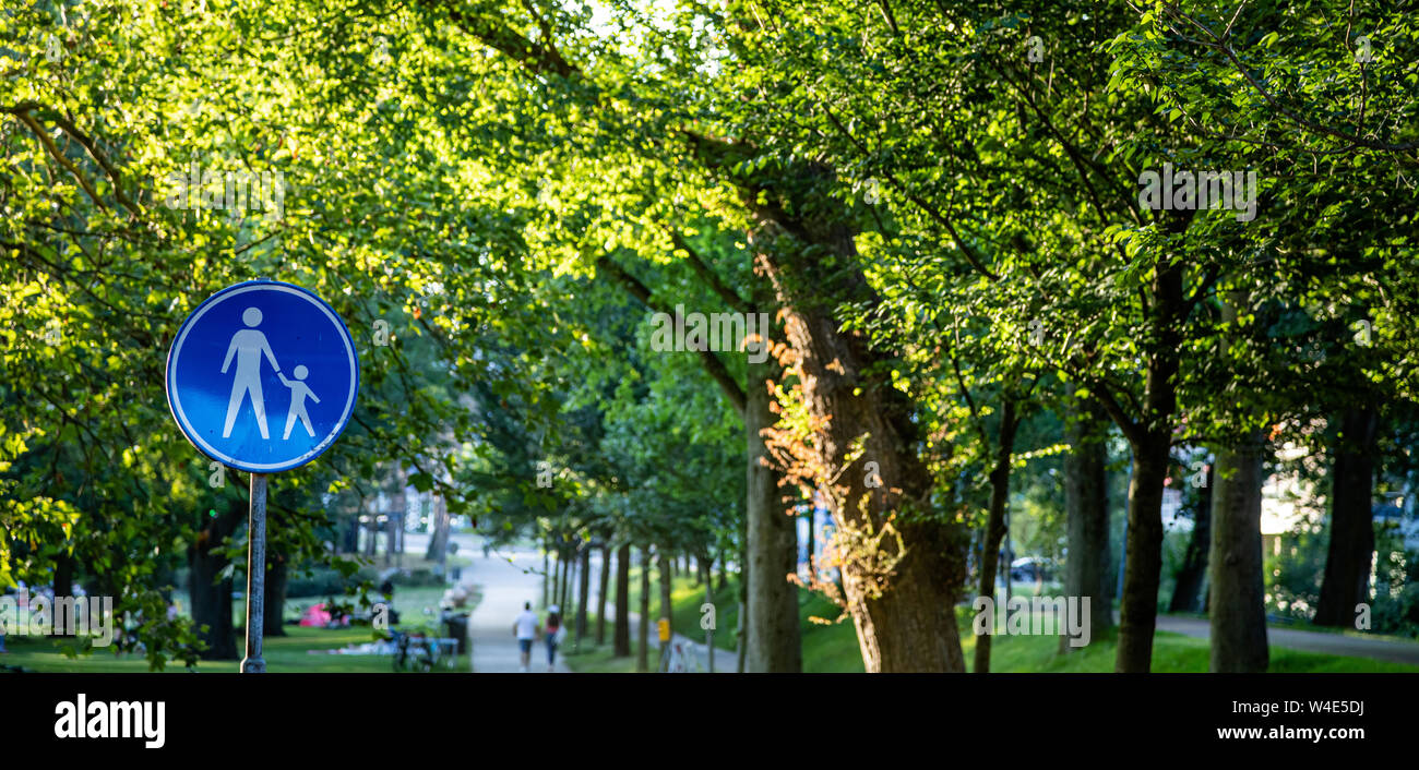 Achtung, Kinder überqueren. Weiße Mutter mit einem Kind Symbol auf runde blaue Farbe, grüne Bäume im Freien Hintergrund. Niederländische Verkehrszeichen, Rotterdam Stockfoto