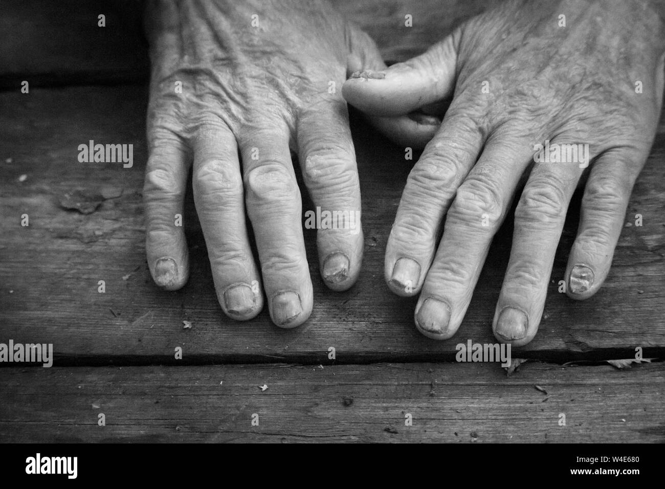 Schwarz-weiß Foto des alten kranken Mann die Hände auf eine antike raue Holz- Oberfläche, Konzept der beging und um Hilfe zu bitten Stockfoto