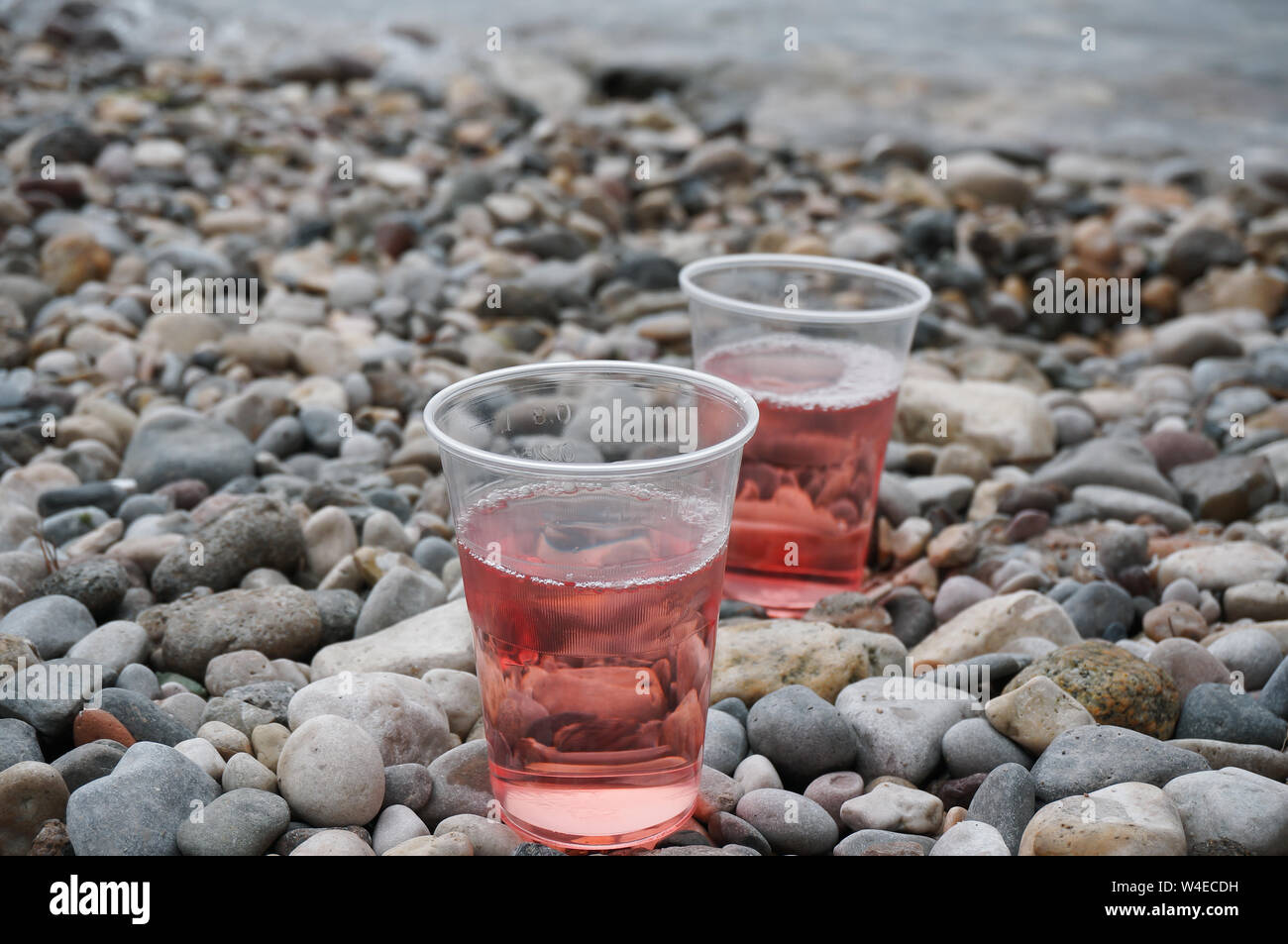 Zwei Plastikbecher von Rose Wein auf Kiesstrand Nahaufnahme Stockfoto