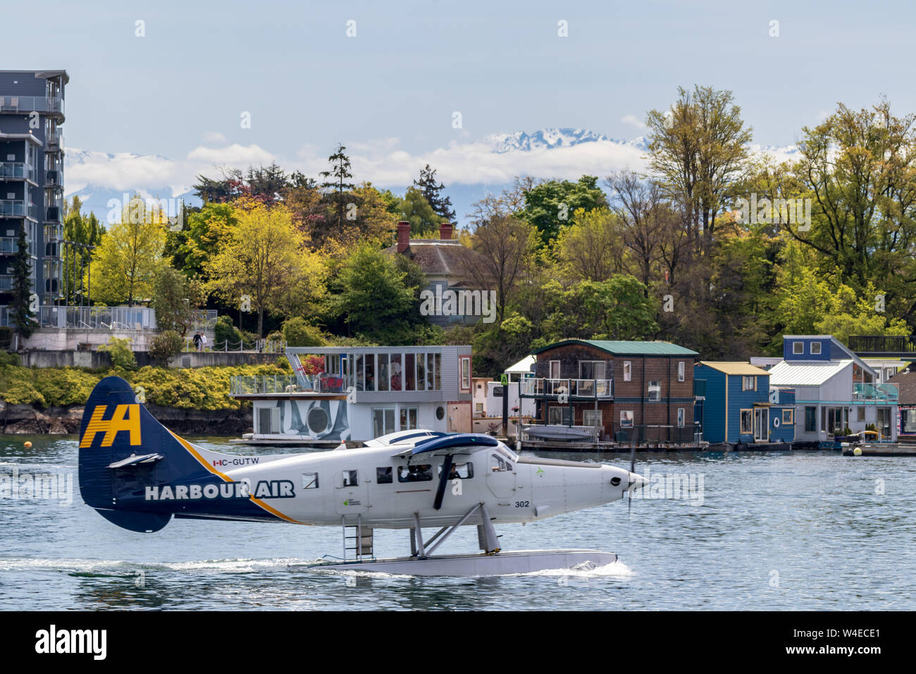 Harbour Air Wasserflugzeug zum Abflug aus Downtown Victoria rangieren mit Bäumen und schneebedeckten Berge im Hintergrund. Stockfoto