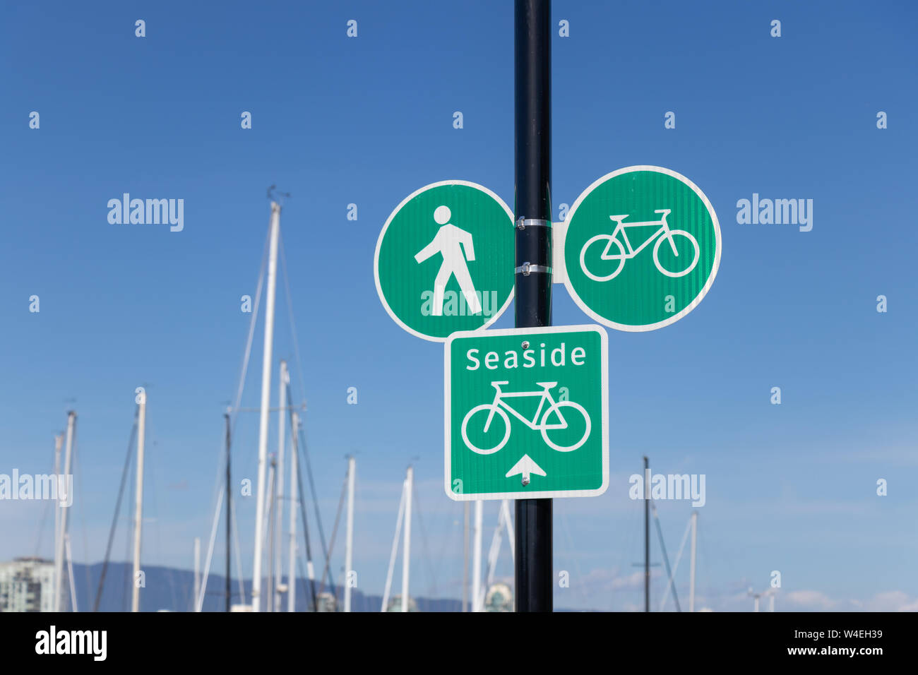 Spazierweg am Meer und ein Schild mit dem Radweg neben einem belebten Yachthafen. Stockfoto