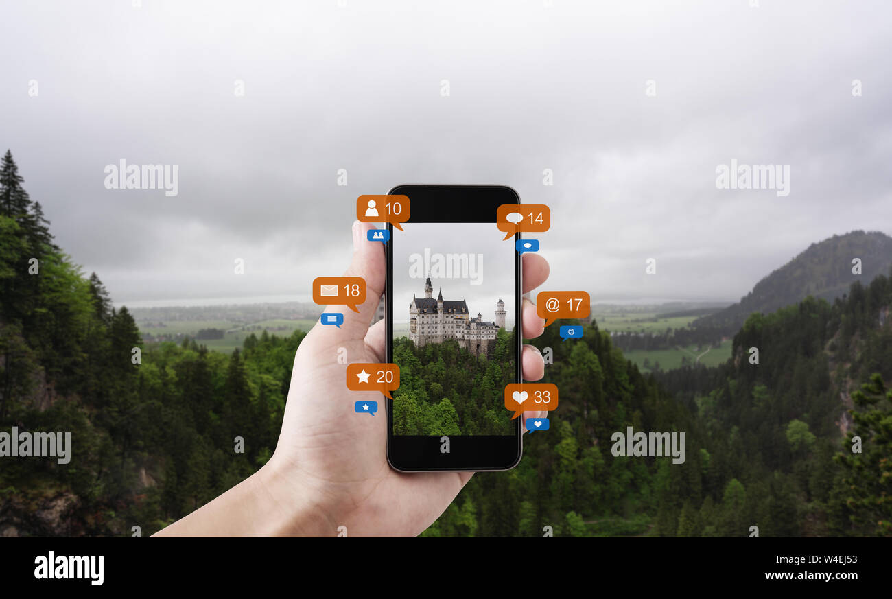 Hand mit smart phone unter Foto von Schloss Neuschwanstein in Deutschland, mit Social Media und Social Network Benachrichtigungssymbole Stockfoto