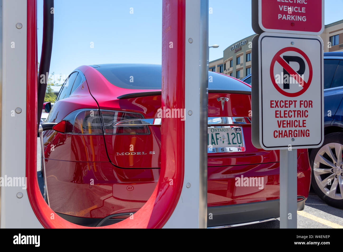 Red Tesla Model S geparkt, das Aufladen bei Tesla Kompressor mit Parkplatz Einschränkung Zeichen hinter dem Fahrzeug. Stockfoto