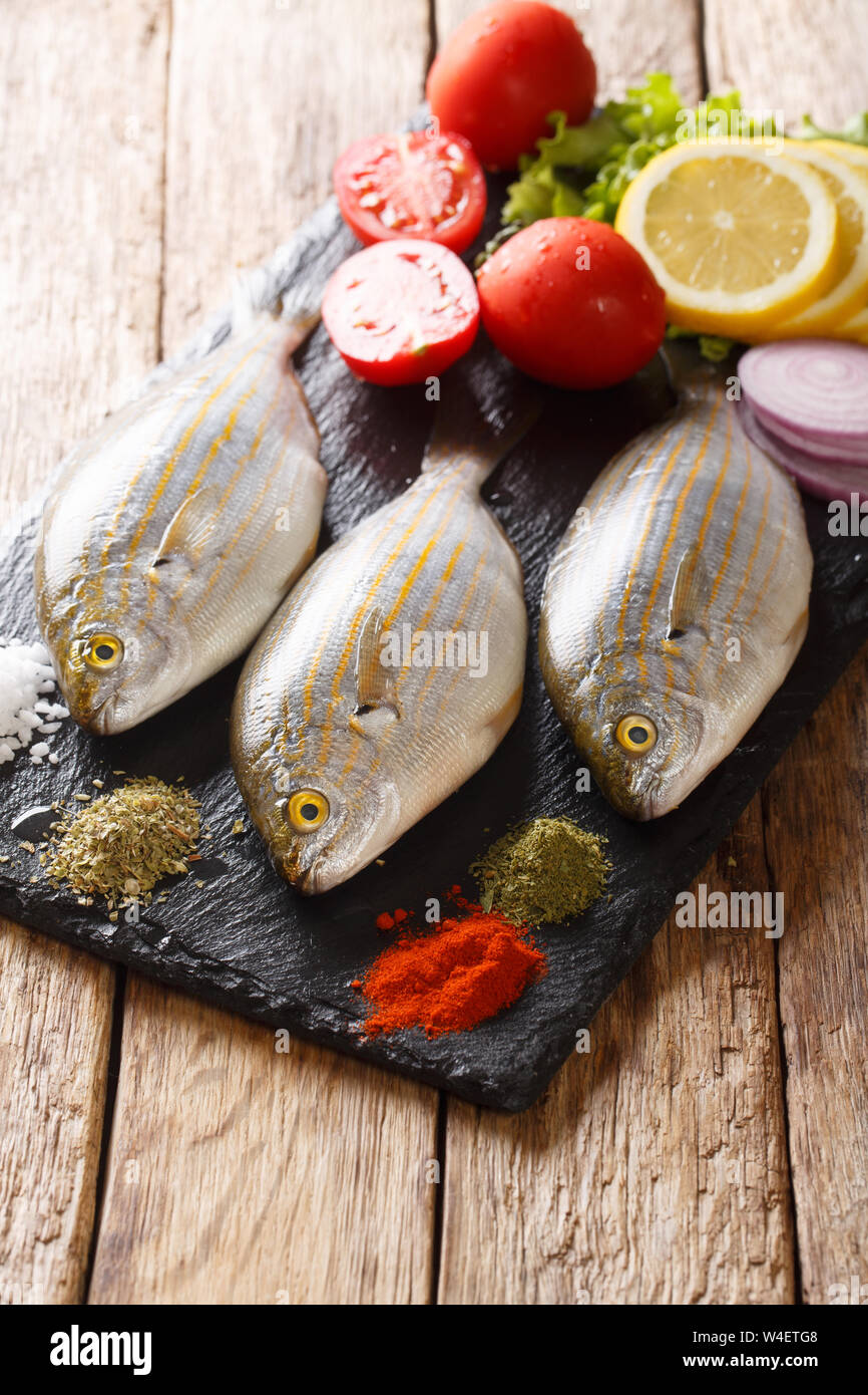 Vorbereitung für das Kochen Sarpa salpa Fisch mit Zitrone, Gemüse und Gewürze close-up auf einer Schiefertafel Board auf dem Tisch. Vertikale Stockfoto