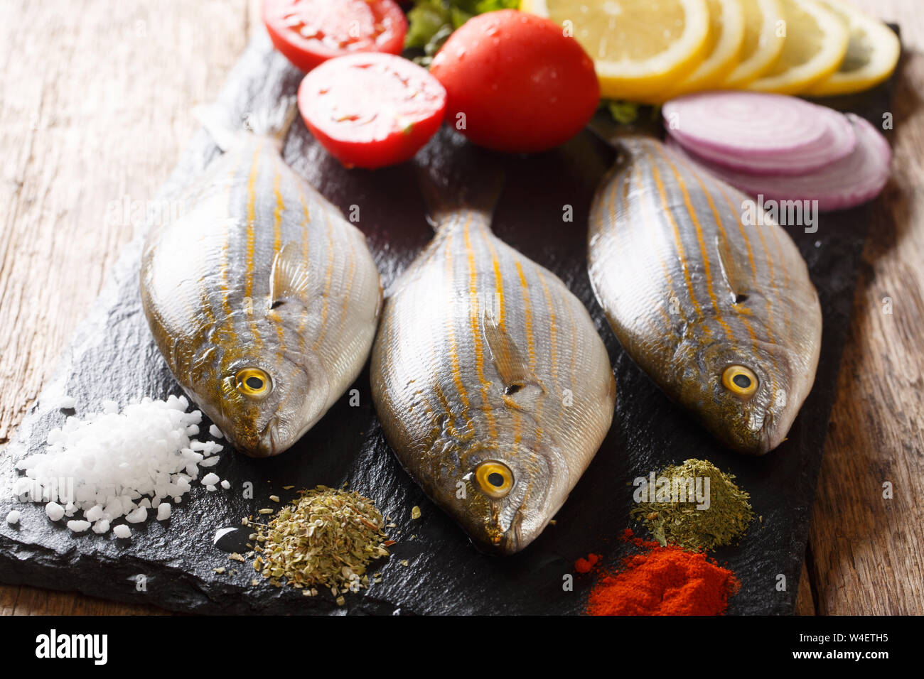 Frische rohe Rohe sarpa salpa Fisch mit Zitrone, Gemüse und Gewürze closeup auf einer Schiefertafel Board auf einen Tisch. Horizontale Stockfoto