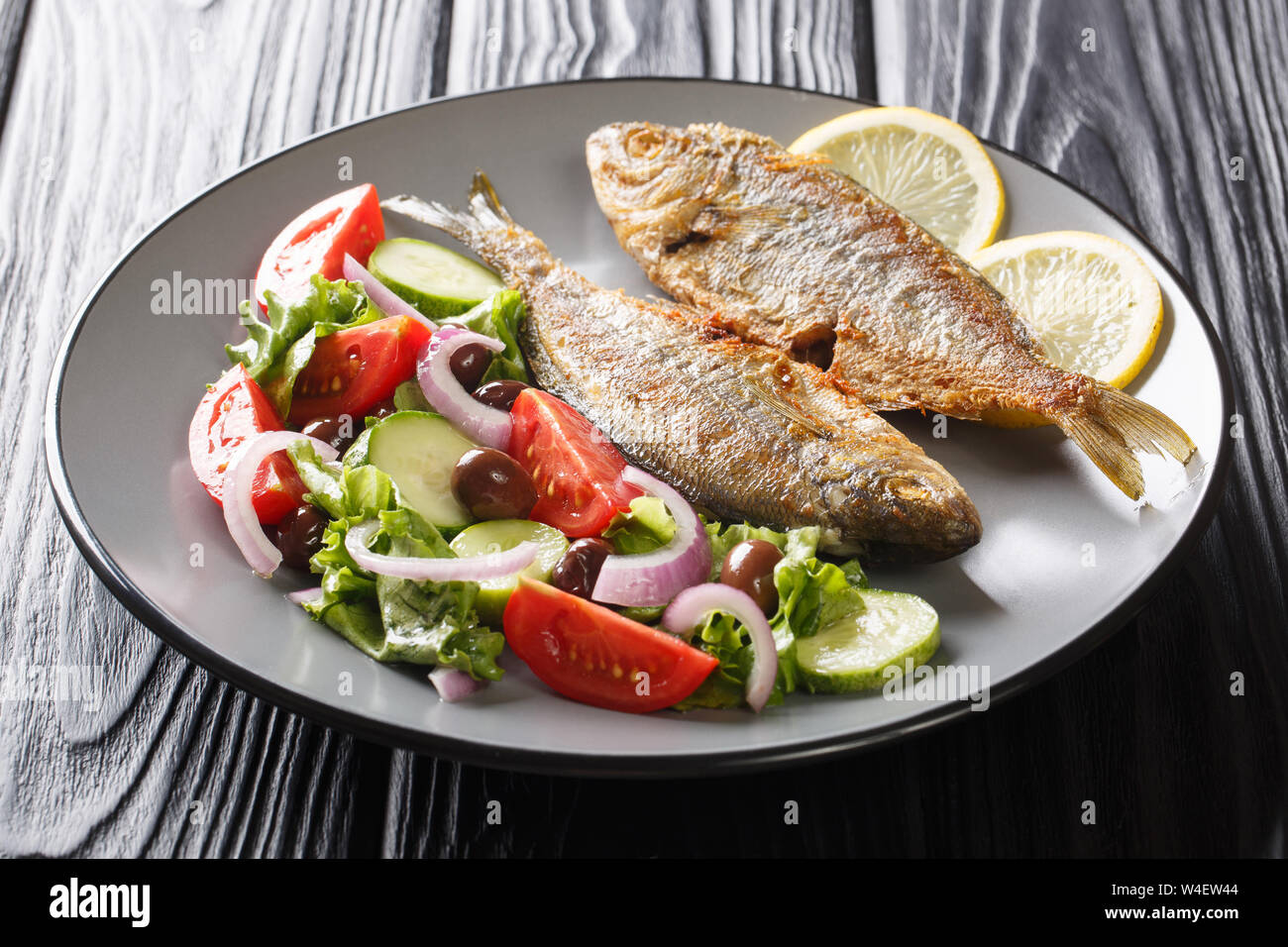 Teil der Fried Salema porgy Fisch mit Zitrone und frischen Salat close-up auf einem Teller auf den Tisch. Horizontale Stockfoto