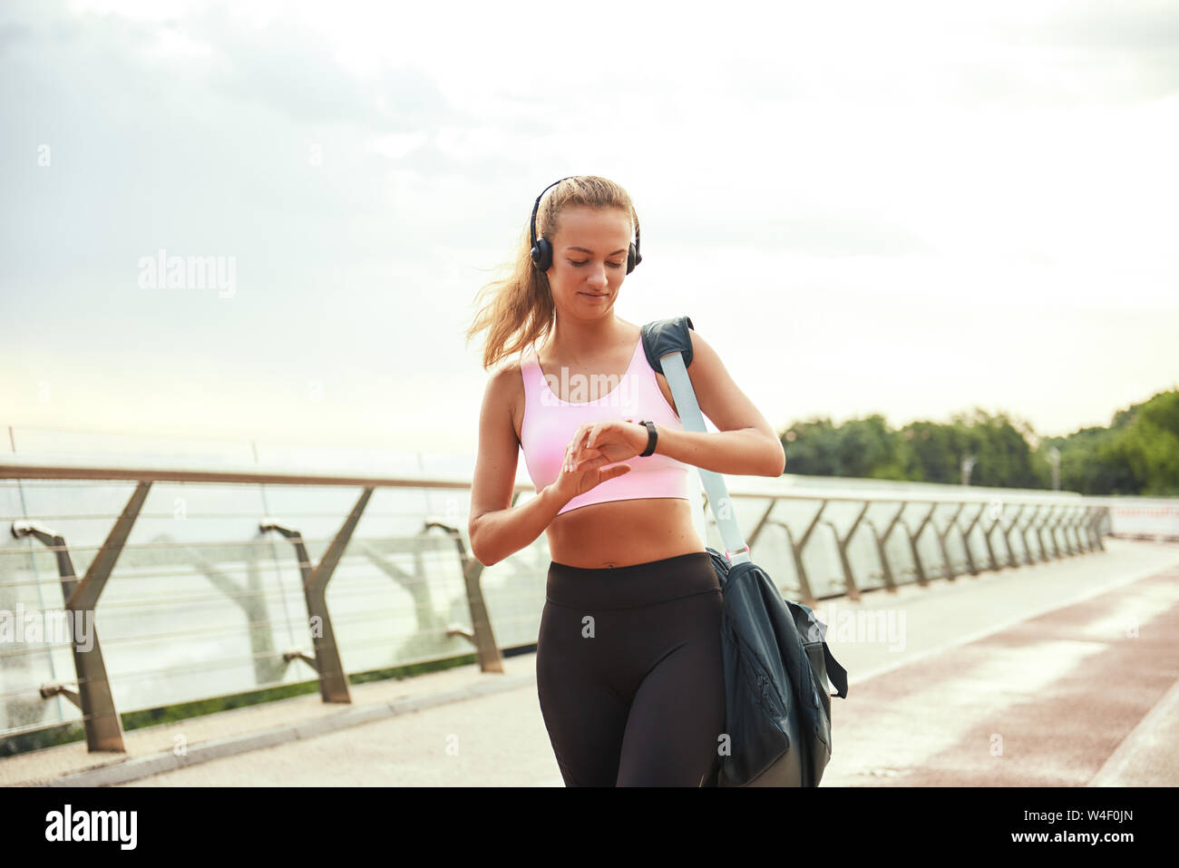 Es war toll trainieren Junge sportliche Frau, Kopfhörer, Tragetasche und Kontrolle der Zeit auf ihrem Ansehen, während auf der Brücke stehen. Motivation. Gesunde Lebensweise. Sport Konzept Stockfoto