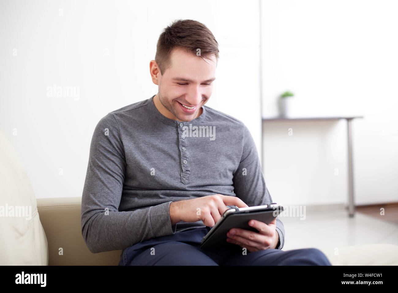 Stattlicher Mann mit digitalen Tablet, sitzen auf der Couch und lächelnd Stockfoto