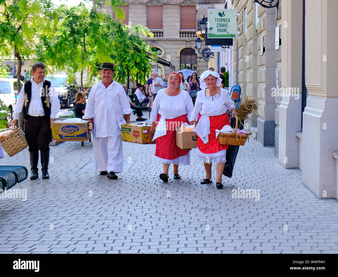 Zagreb, Kroatien. Gruppe von Menschen, die weiß gekleidet in traditionelle Outfits zu Fuß auf der Straße in der Stadt mit der Landwirtschaft und Kochutensilien. Stockfoto