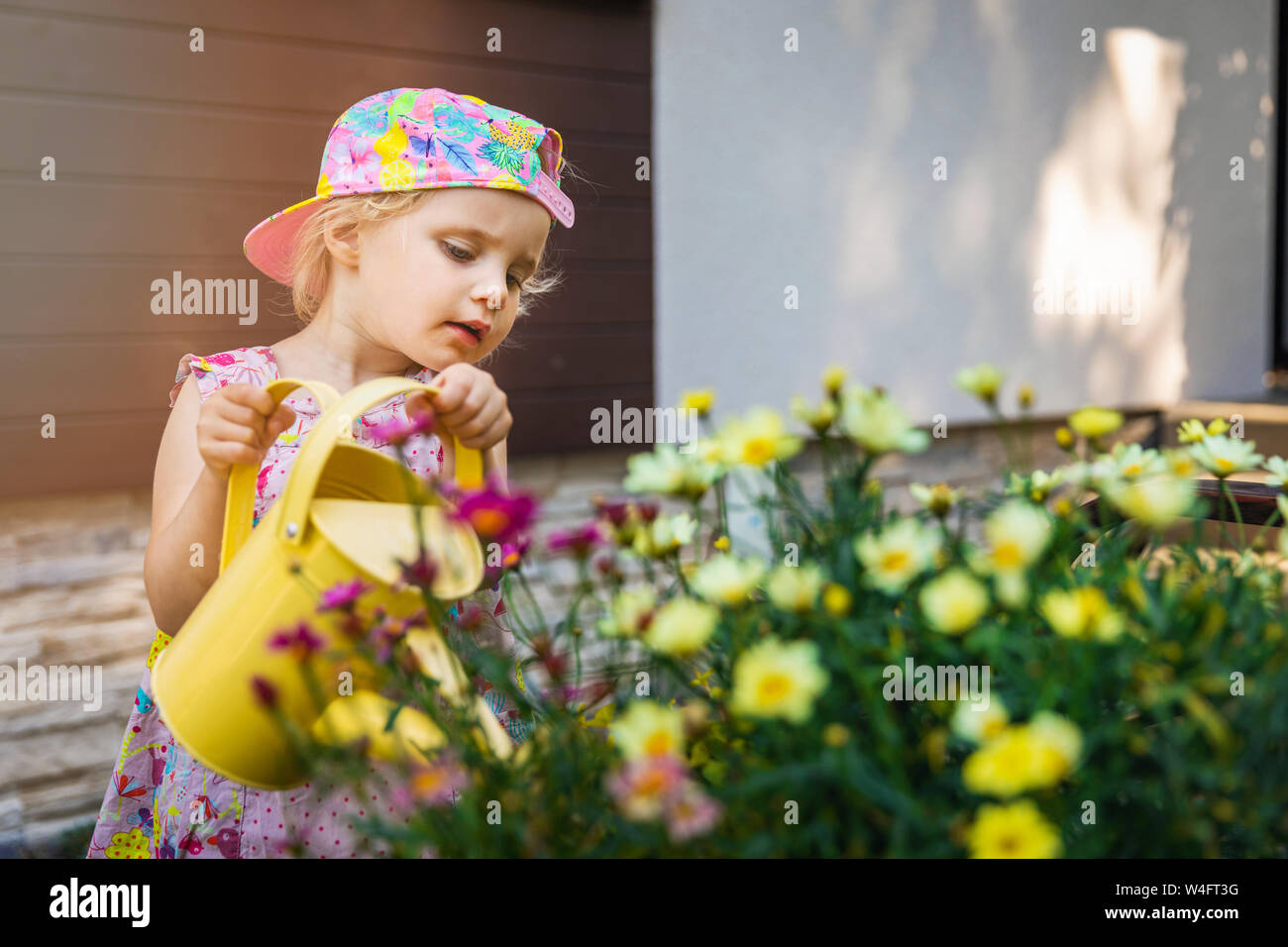 Kleines Mädchen Blumen gießen mit gelben Gießkanne vor dem Haus Stockfoto