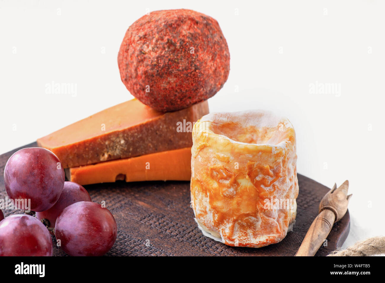 Feinkost würzige Käsesorten verschiedener Sorten. Roter Cheddar, blauer Dor, Pyramide, Stilton, Belper-Noll auf einer braunen Keramikplatte mit Trauben. Würzig Stockfoto