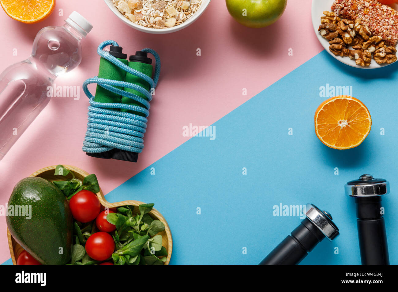 Blick von oben auf die Diät Nahrung, Wasser, Springseil und Hanteln auf Rosa und blauen Hintergrund Stockfoto