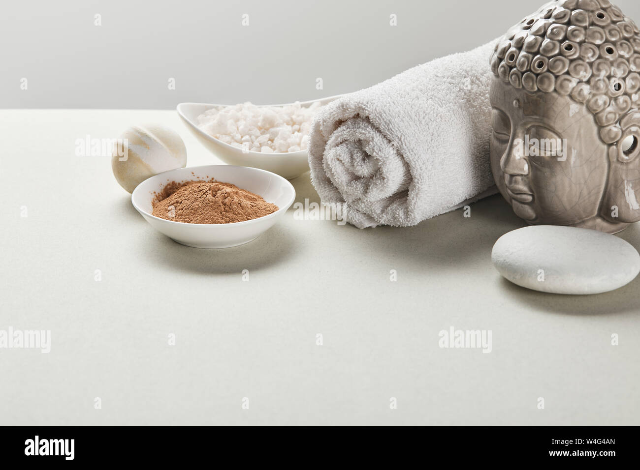 Meersalz und Lehm Pulver in Schalen, Baumwolle Handtuch, Stein, Badebombe  und Buddha Figur am weißen Tisch isoliert auf Grau Stockfotografie - Alamy