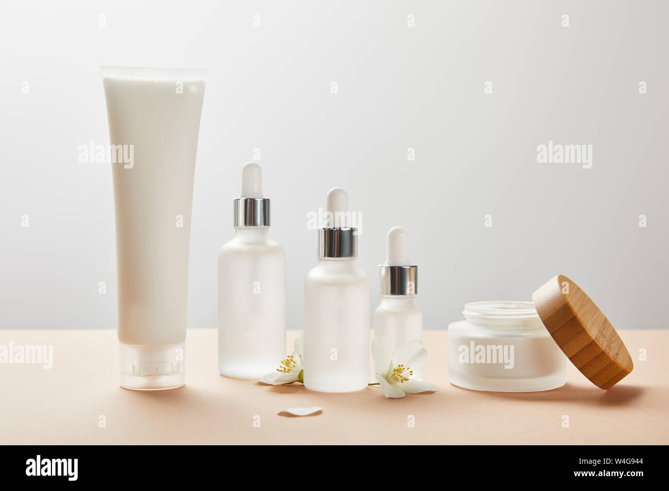 Creme Tube, kosmetischen Glasflaschen, öffnen Sie jar mit Sahne und paar Jasminblüten auf beige Stockfoto