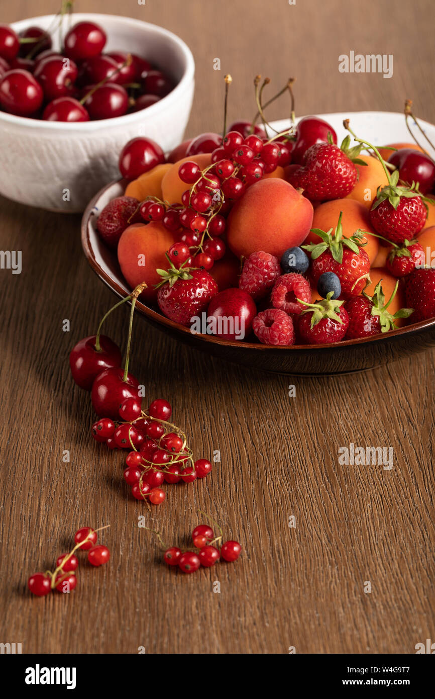 Selektiver Fokus der roten Kirschen in Weiß Schüssel und gemischte Beeren auf Platte auf hölzernen Tisch Stockfoto