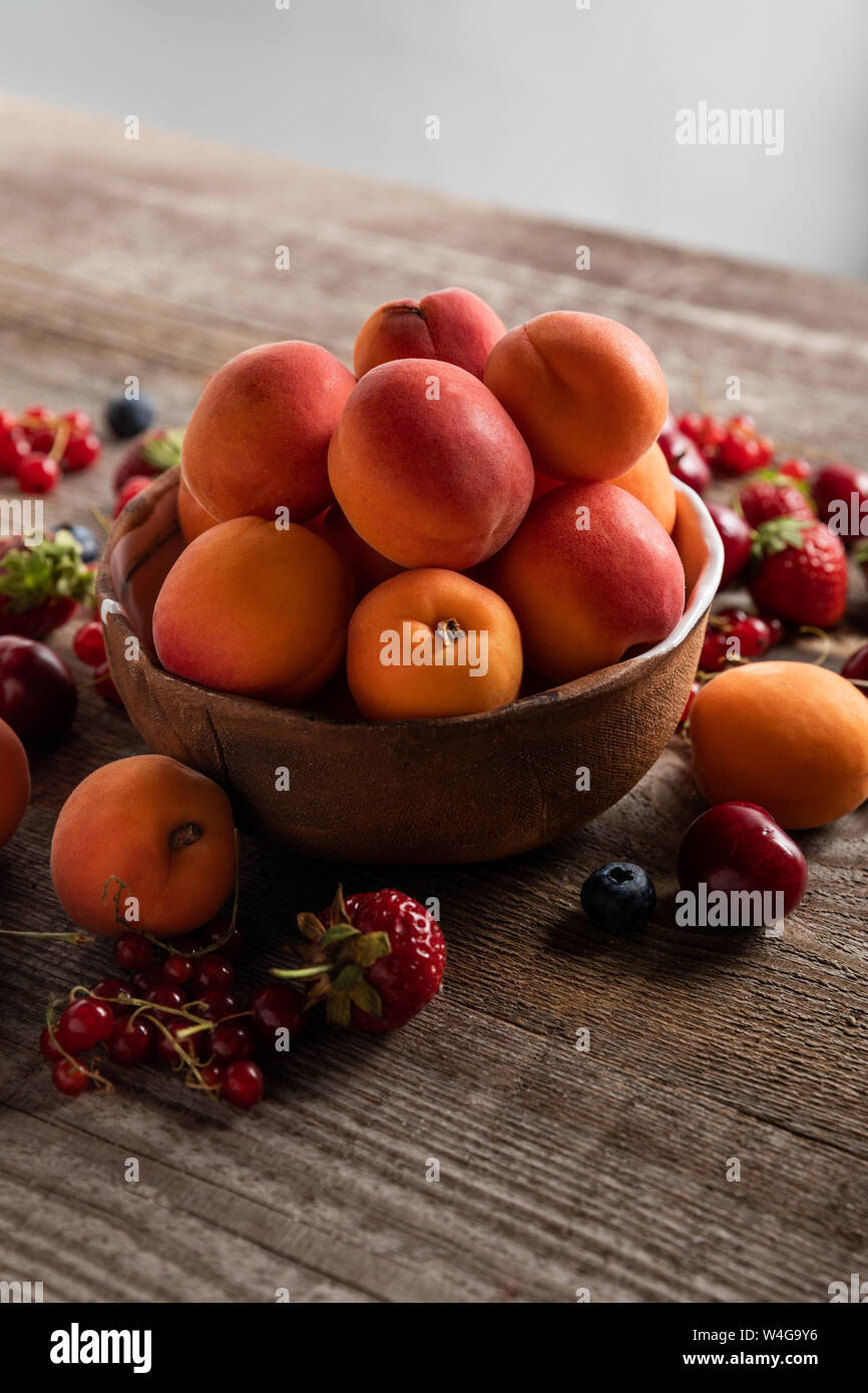 Reifen köstliche saisonale Beeren um Schale mit frischen Aprikosen auf Holztisch isoliert auf Grau verstreut Stockfoto