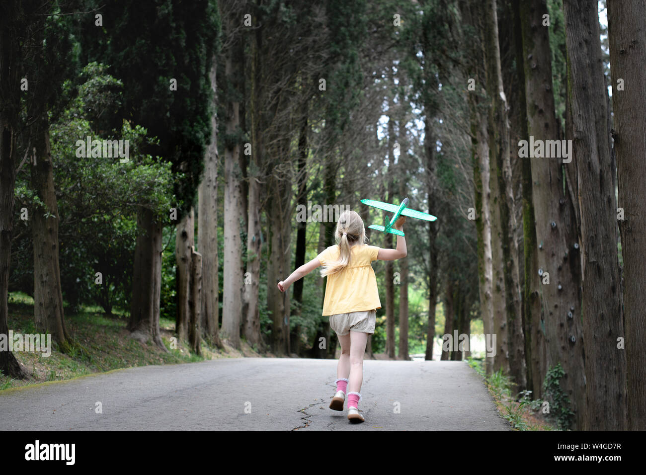 Mädchen mit Flugzeug, auf einer kleinen, mit Bäumen gesäumten Straße Stockfoto