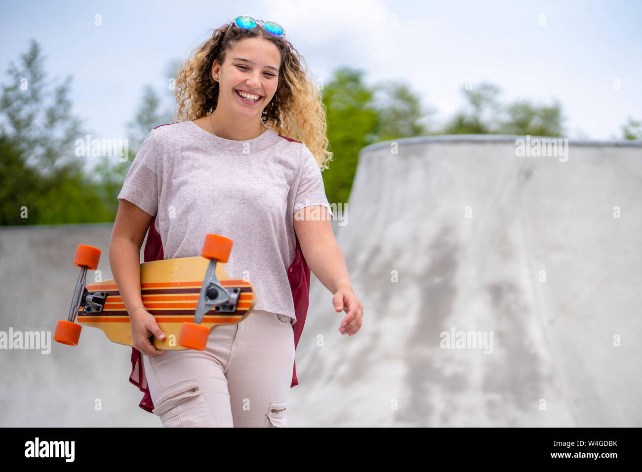 Lächelnde junge Frau mit einem Longboard in einem Skatepark Stockfoto