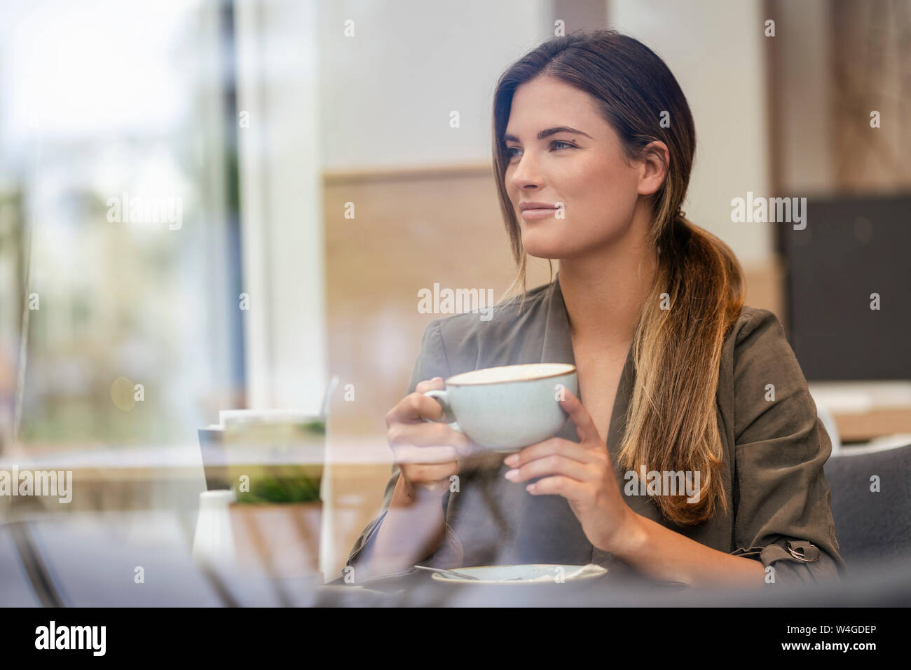 Junge Geschäftsfrau mit Tasse Kaffee in einem Cafe, durch das Fenster gesehen Stockfoto