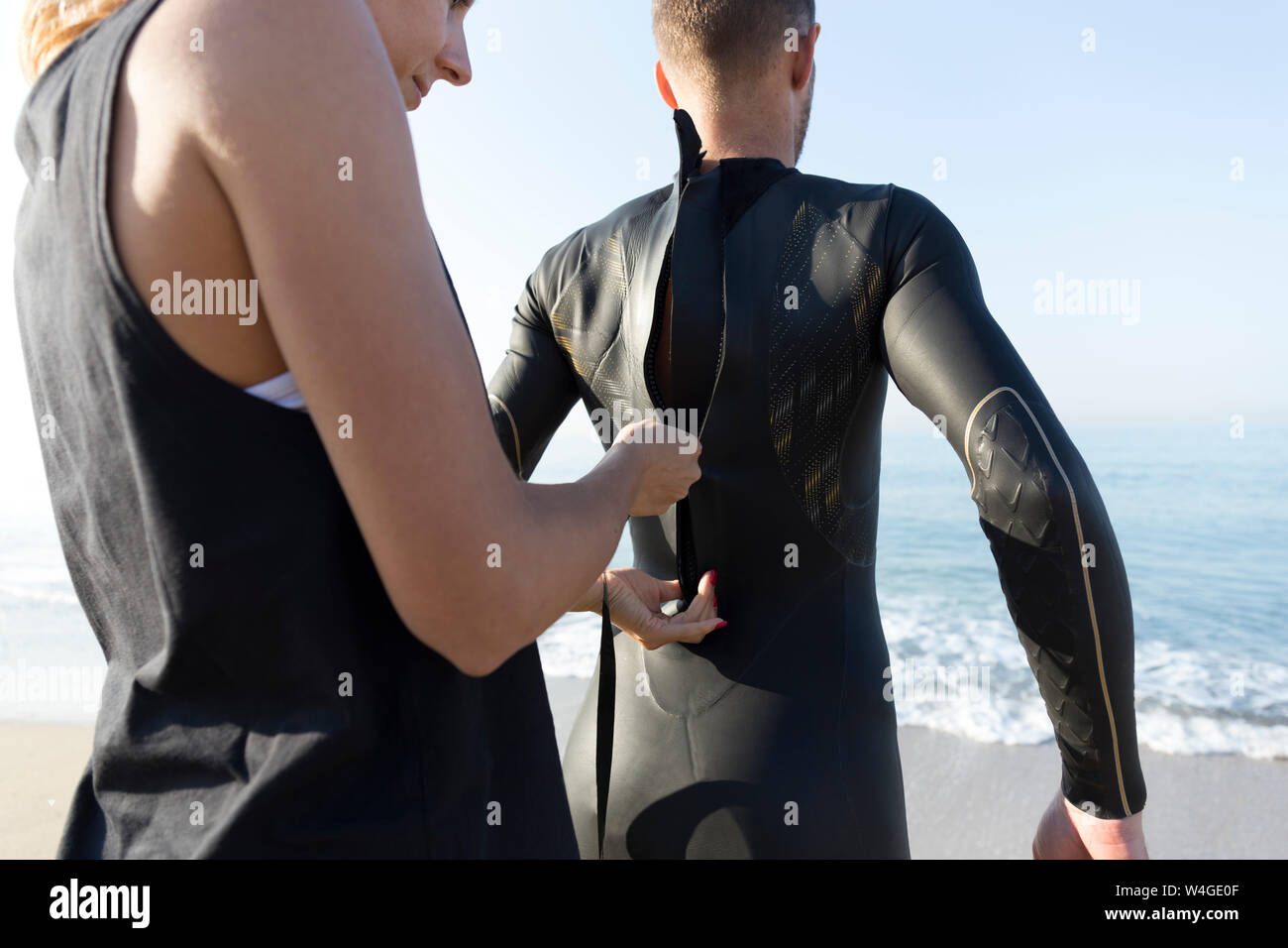 Frau zipping up Anzug der Mann am Strand Stockfoto