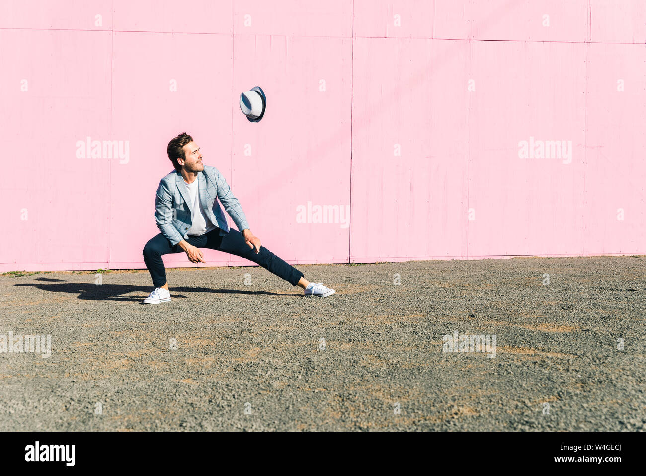 Junger Mann vor rosa Bau Barriere, seinen Hut fliegen in den Wind beobachten Stockfoto