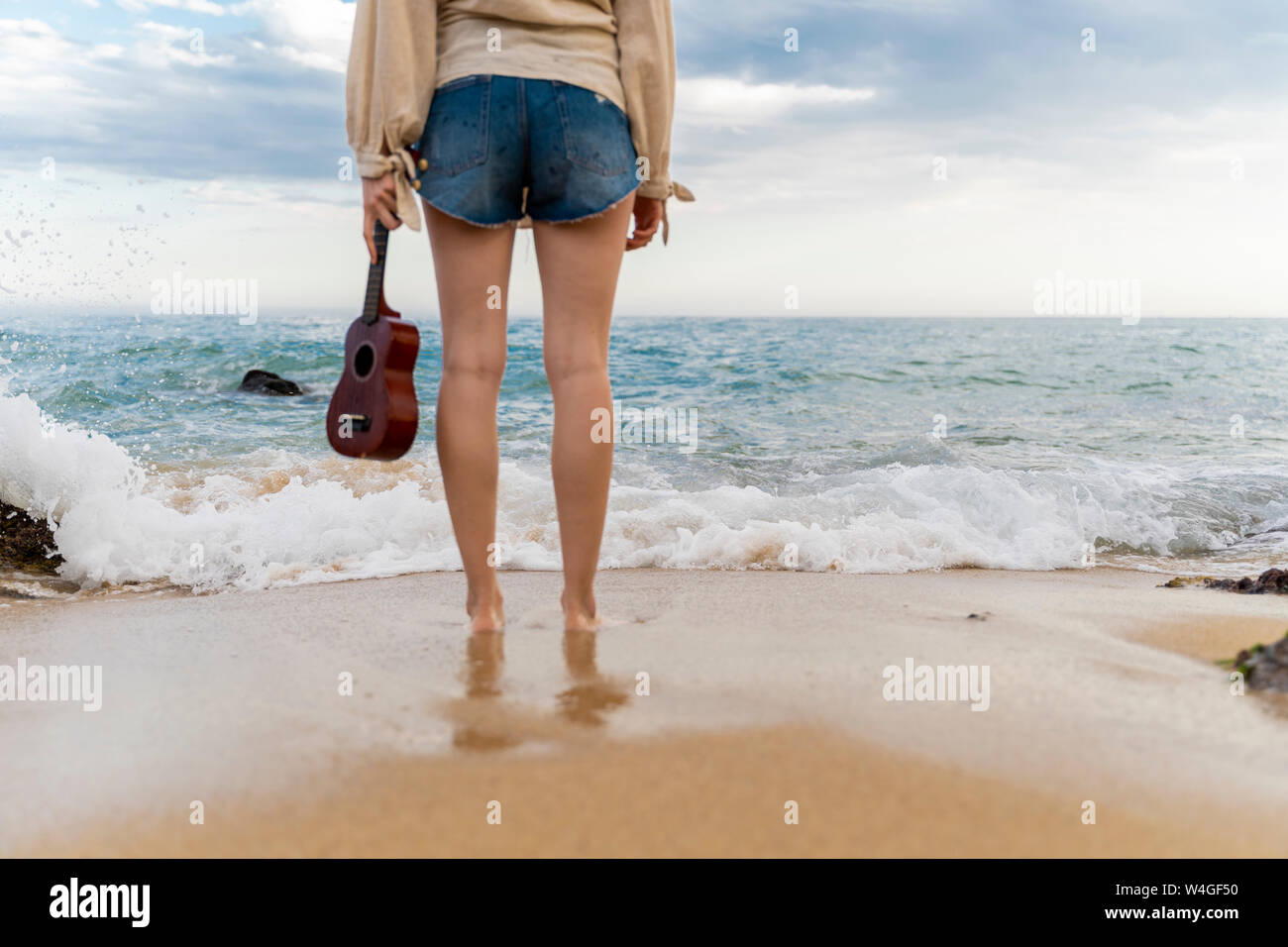 Frau mit Ukulele stehend vor dem Meer, Teilansicht Stockfoto