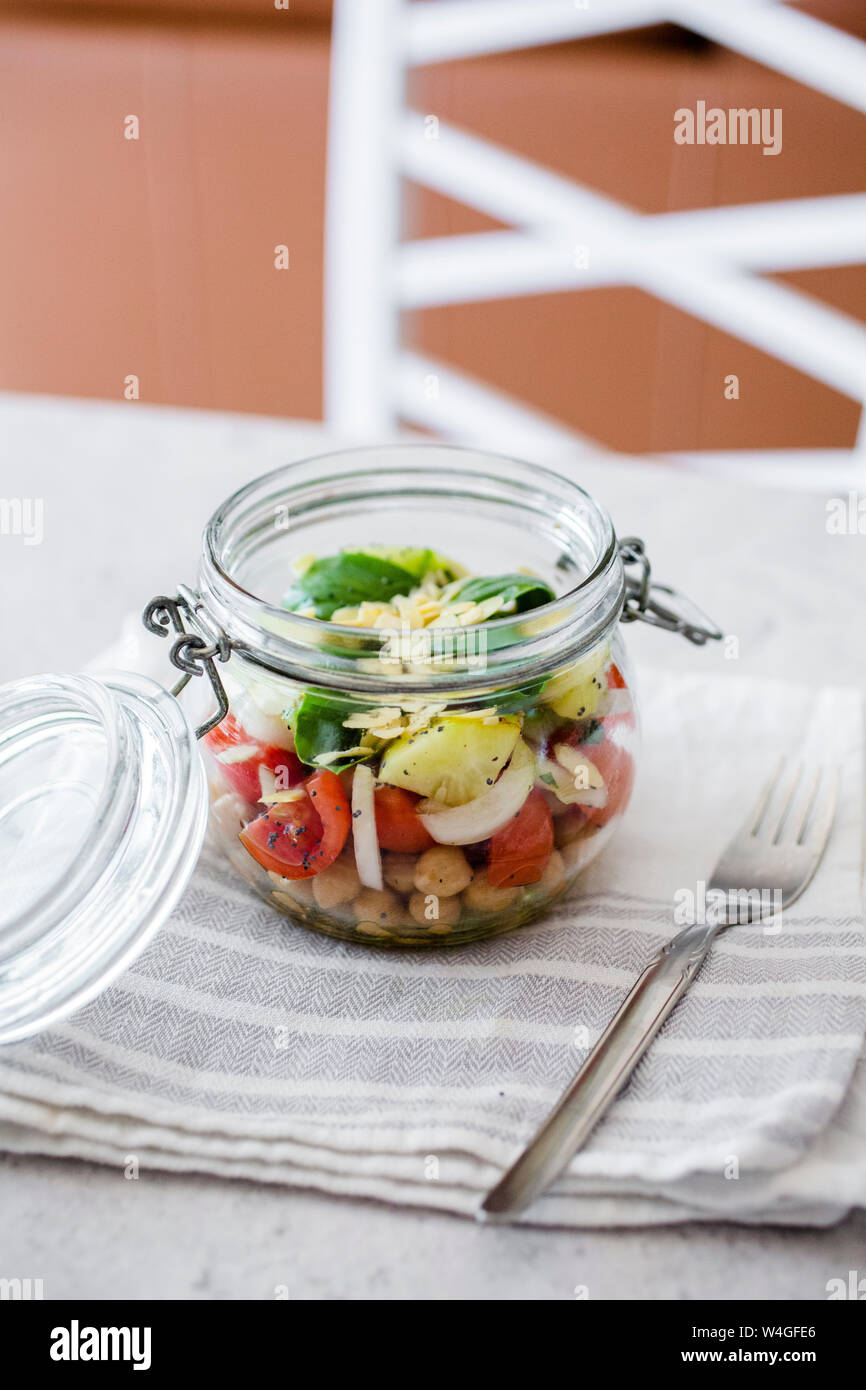 Glas Salat mit Gurken, Kichererbsen, Zwiebeln, Tomaten, Basilikum, Chia Samen und gehobelten Mandeln Stockfoto